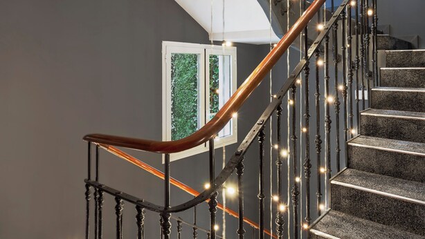 Un escalier doté d’une main courante en bois et de balustrades en métal, décoré de guirlandes lumineuses.