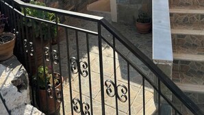 A balcony with a stone staircase, potted plants, and a view of a building with blue doors. - Ruby Apartment (Αγιος Νικολαος)