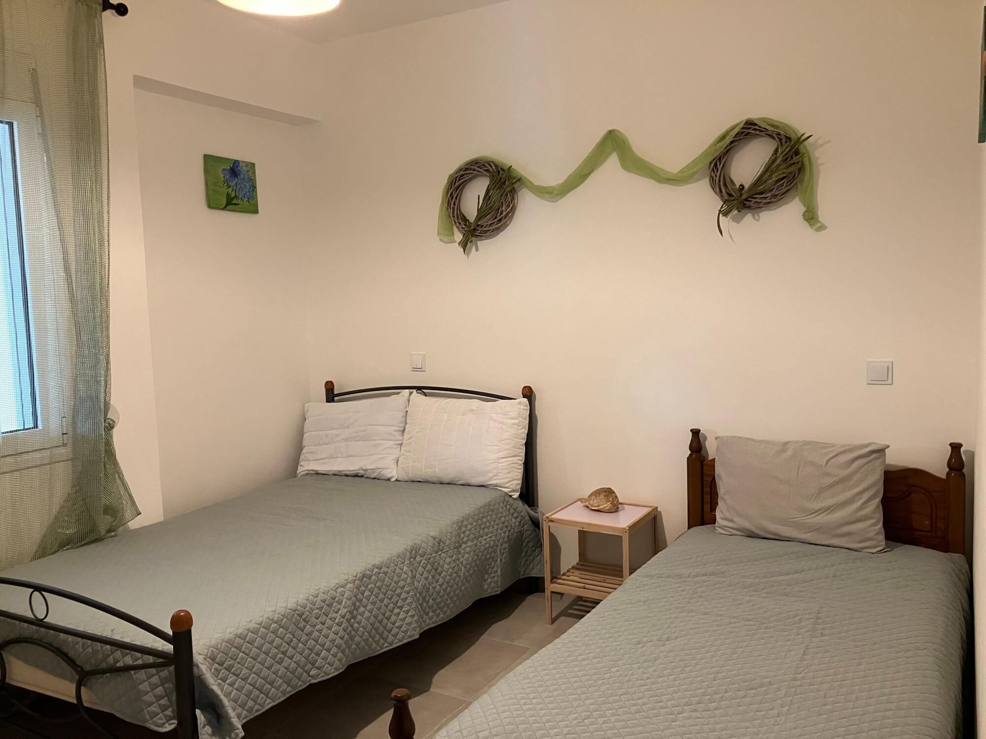 A bedroom with two single beds, a small bedside table with a lamp, and a wall-mounted wreath decoration.