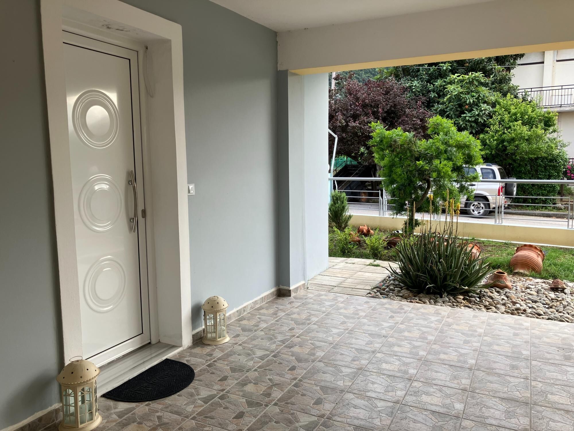Una entrada limpia y moderna con piso de baldosas, una puerta blanca y un pequeño jardín con plantas y un farol.