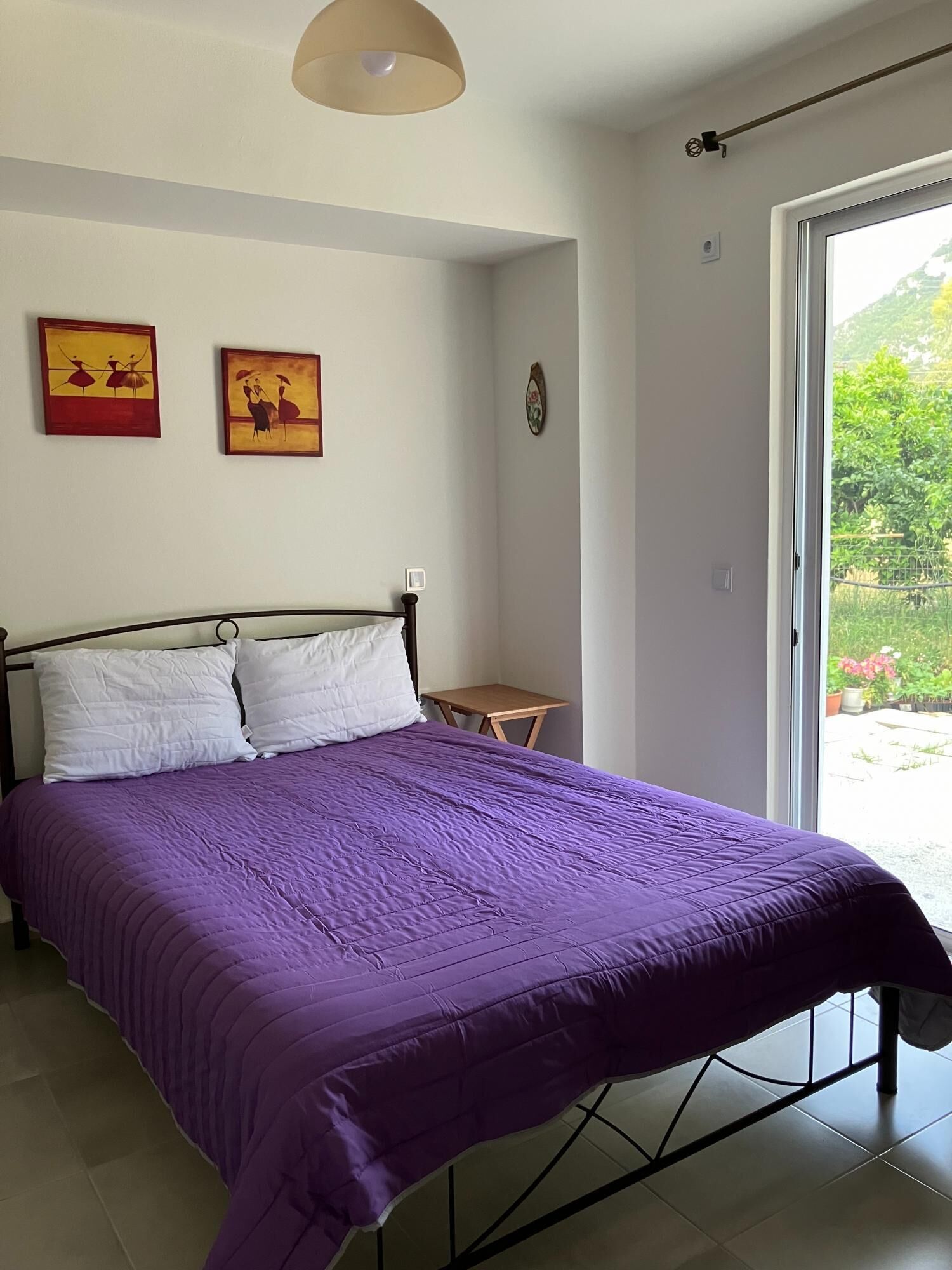 A bedroom with a bed, a small table, and two paintings on the wall.