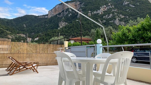 Una terraza con sillas de plástico blanco y una mesa, con vistas a un paisaje montañoso.