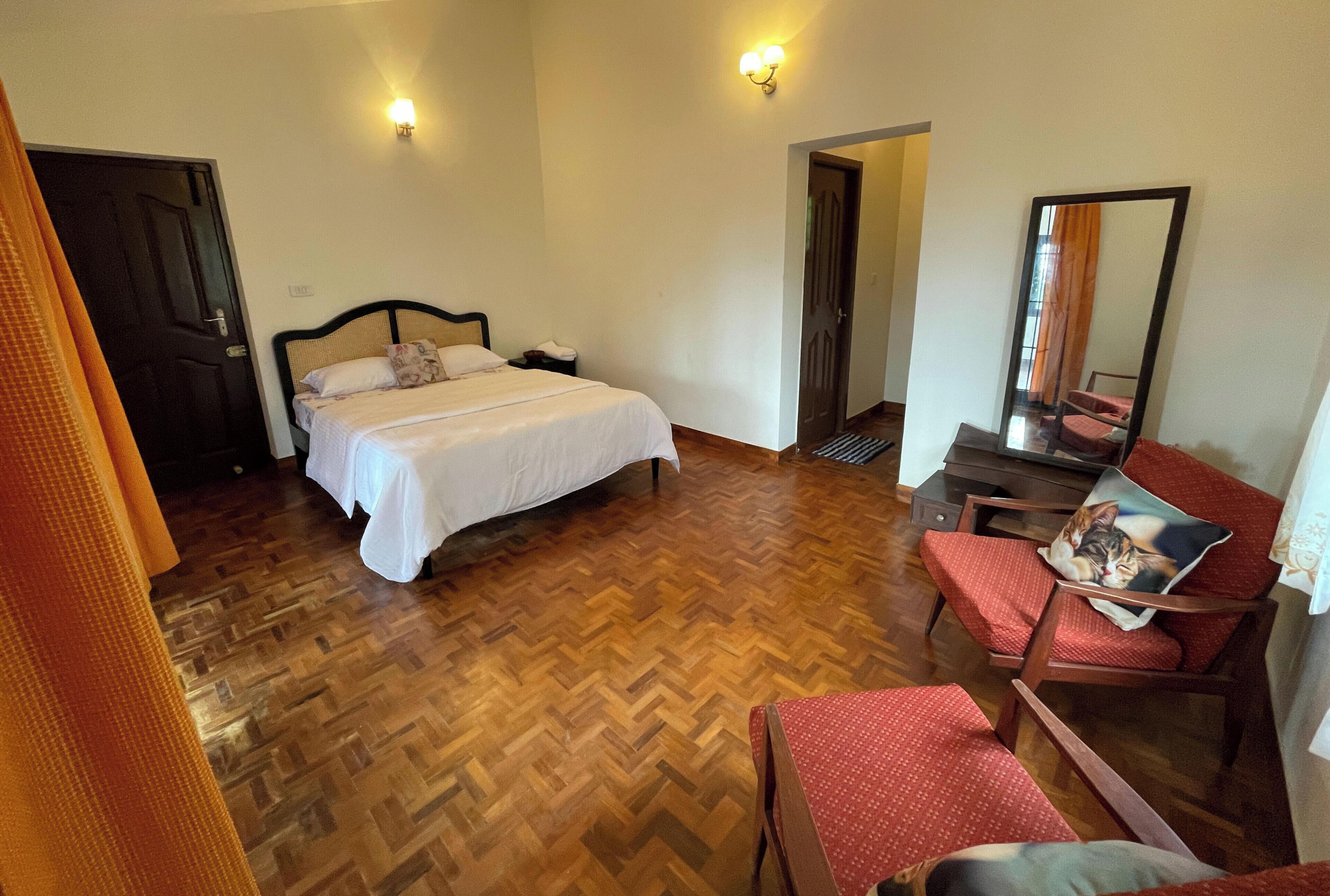 A hotel room with a bed, a desk, a chair, a mirror, and a door.