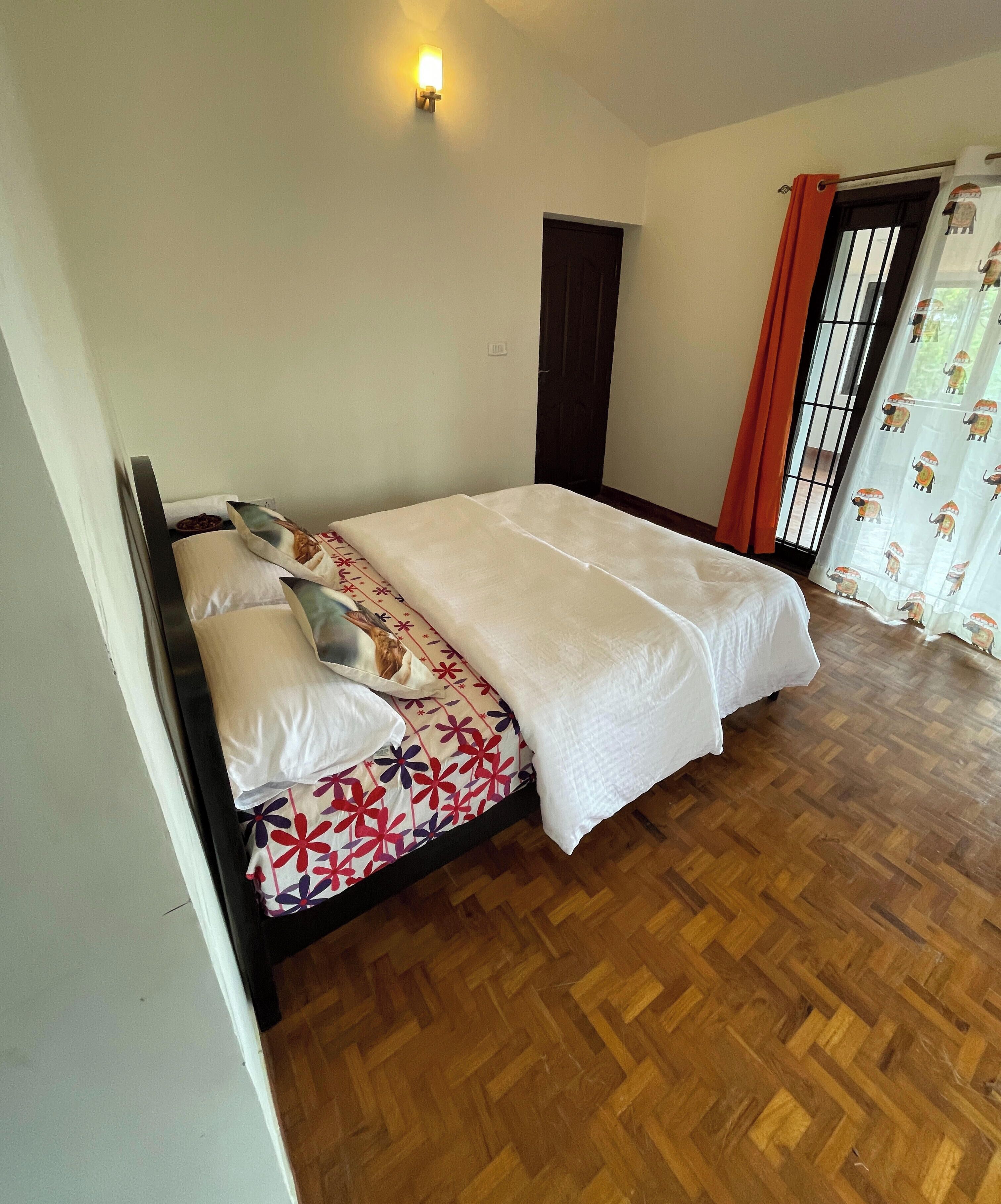 Un dormitorio con cama, luz empotrada, una puerta y un ventanal con cortinas.