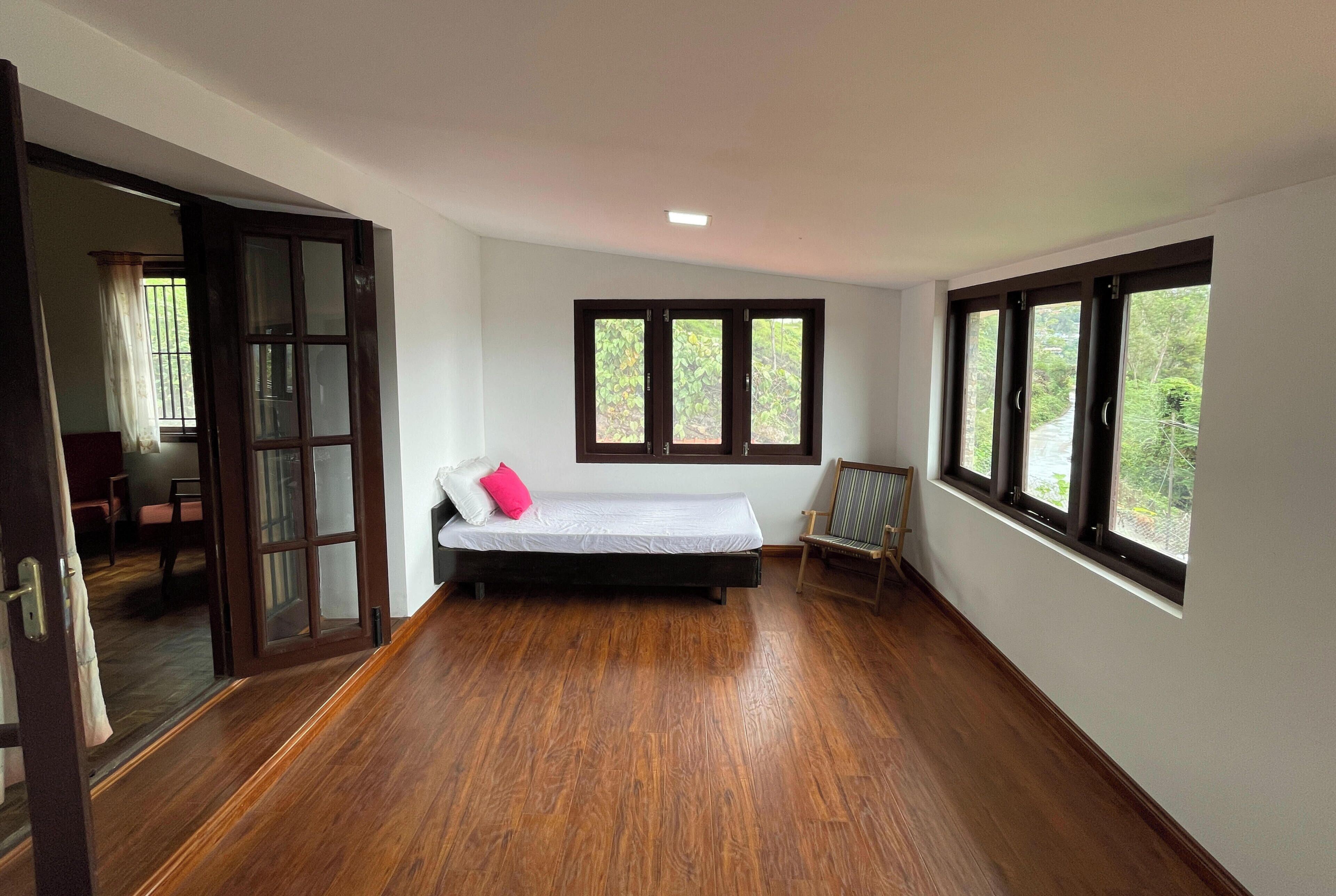 Una habitación con una cama, un sillón y ventanas amplias.