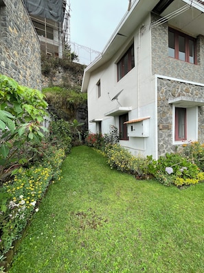 A modern house with a stone facade, a small garden with various plants and flowers, and a satellite dish. -  Nashika Villa by evaddo (Kodaikanal)