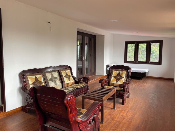 A spacious room with a wooden floor, a sofa set, a small table, and a bed. - Nashika Villa by evaddo stays (Kodaikanal)