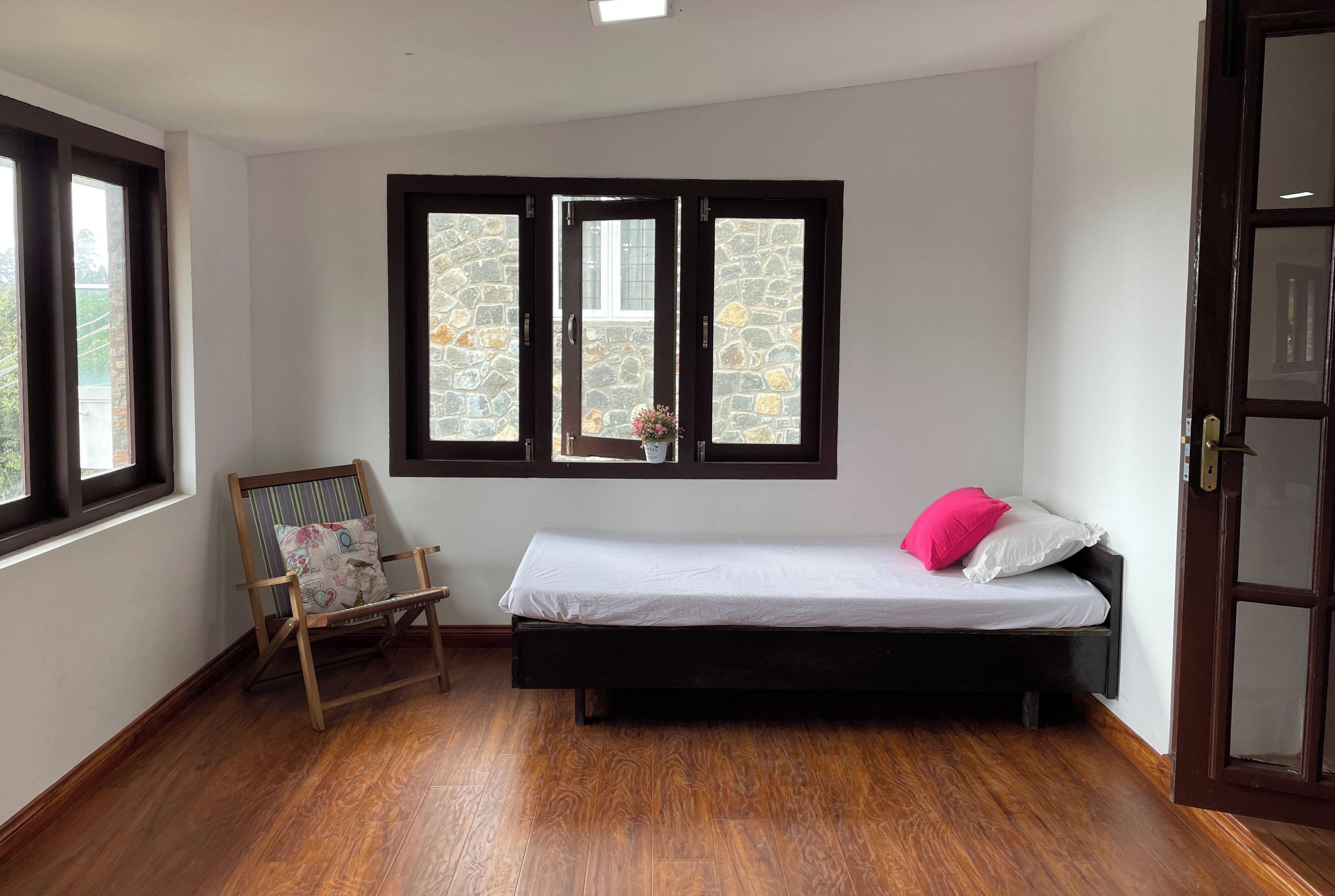 A small, single-bed room with a wooden floor, a rocking chair, and a window with a stone wall view.