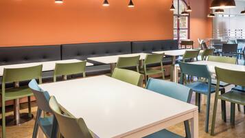 A restaurant with white tables and green chairs, orange walls, and black cushioned seating.