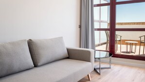 Un salon moderne avec un canapé gris, une table basse en verre et une grande fenêtre donnant sur un patio extérieur.