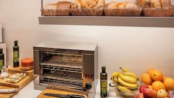 A kitchen with a toaster oven, a cutting board with a knife, a bowl of bananas, a bowl of apples, and a basket of bread.