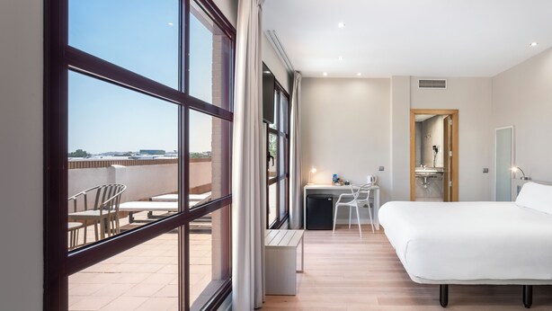 Une chambre d’hôtel moderne avec une grande fenêtre, un lit, un bureau et une chaise.