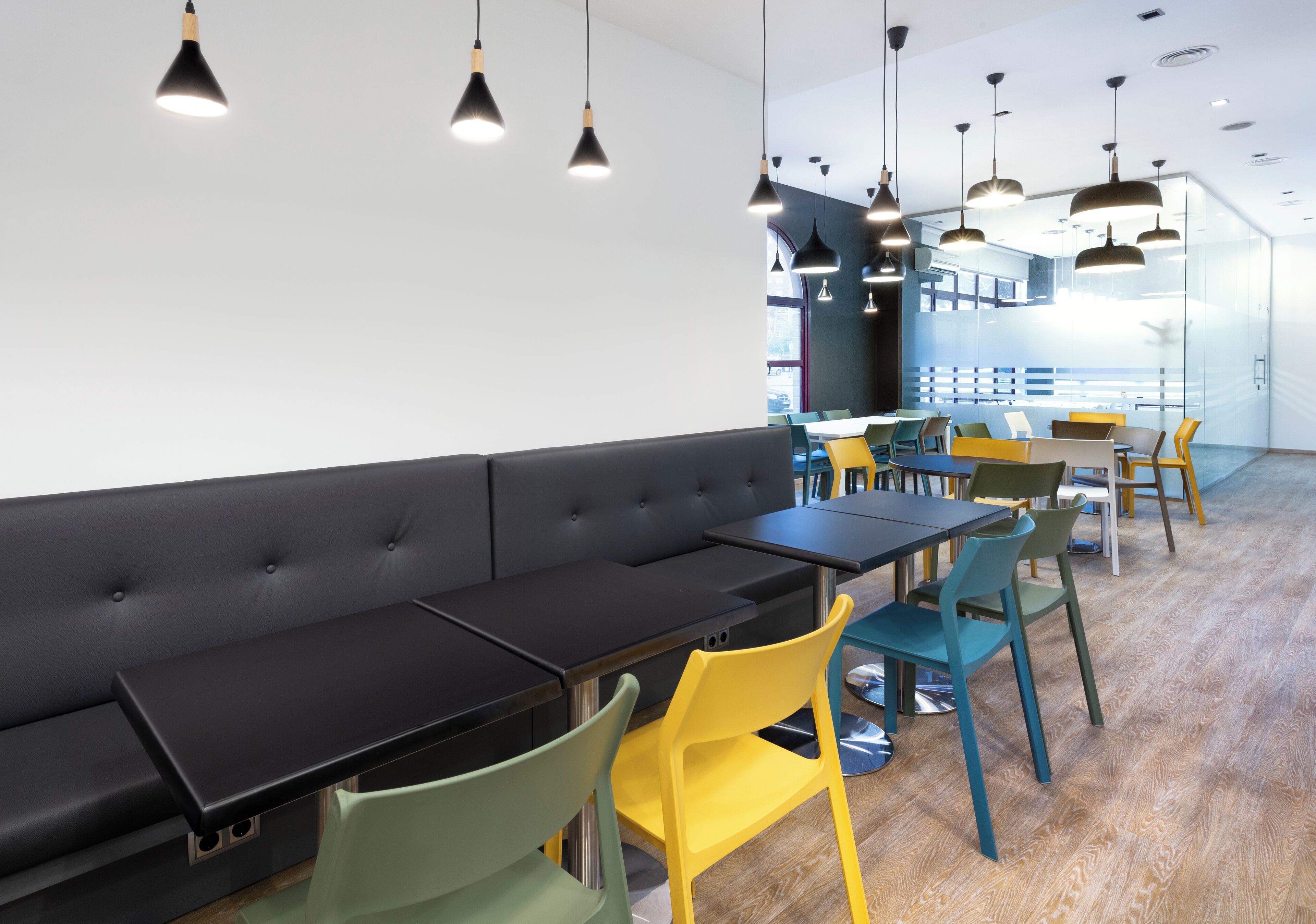A modern dining area with black tables, colorful chairs, and pendant lighting.