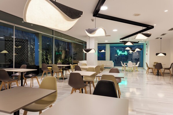 A modern dining area with tables and chairs, large windows, and hanging pendant lights.