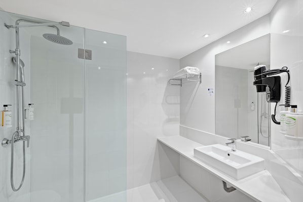 Een moderne badkamer met een douche met glazen wand, een witte wastafel en een haardroger bevestigd aan de muur.
