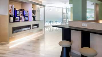 Un espacio moderno de bar con máquinas expendedoras de café, taburetes y un separador de vidrio con texto motivacional.