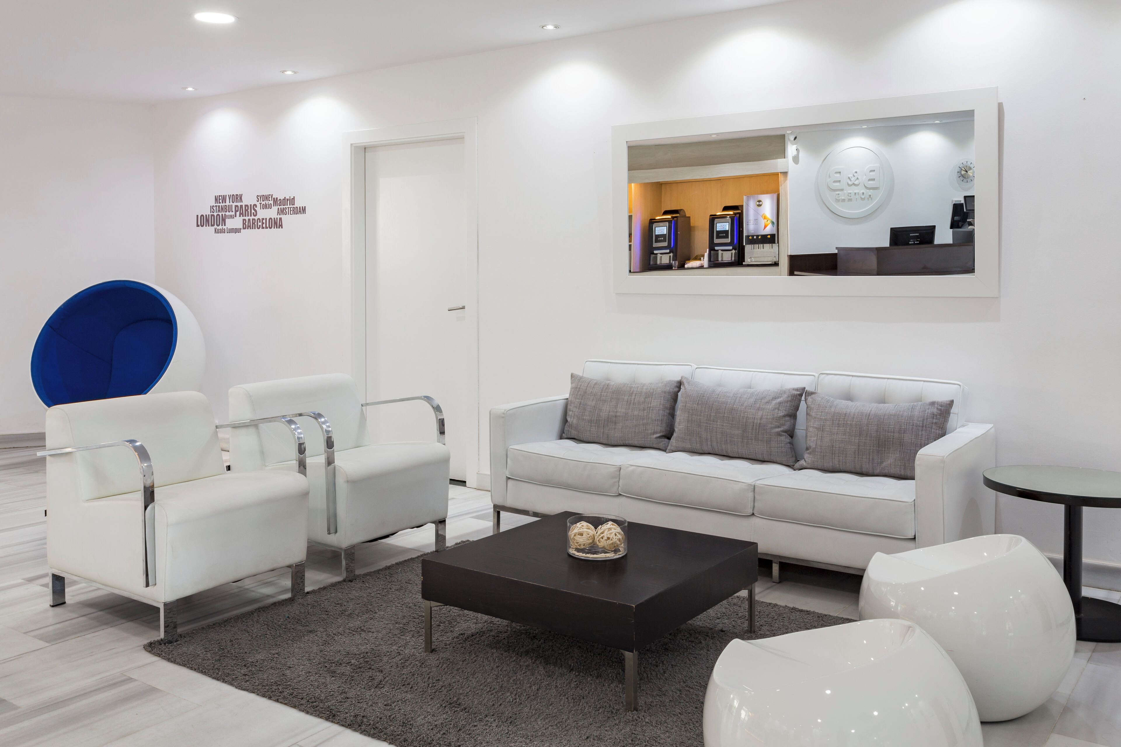A modern hotel lobby with a white sofa, two white armchairs, a black coffee table, and a blue accent chair.