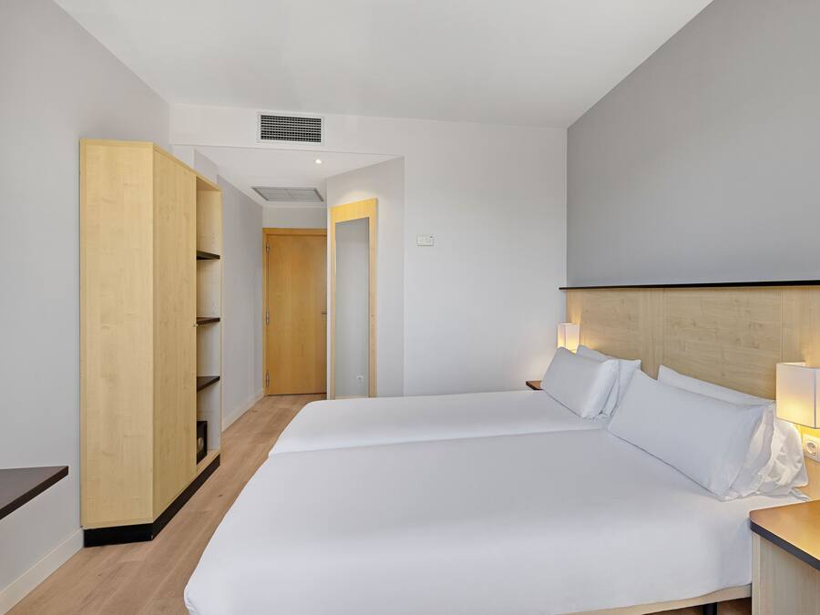 A hotel room with a large bed, a wooden wardrobe, and a bedside table with a lamp.