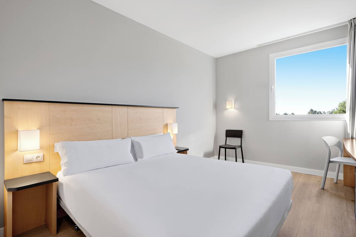 Ein modernes Hotelzimmer mit einem großen Bett, Nachttischen, einem Schreibtisch und einem Sessel.