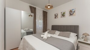 Ein modernes Schlafzimmer mit einem großen Bett, einem Kleiderschrank, einem Nachttisch mit Lampe und einem Fenster mit Vorhängen.
