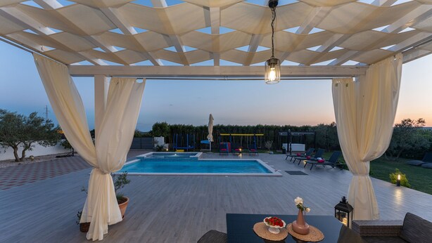 Ein überdachter Außenbereich mit Pool, Sitzgelegenheiten und einem Tisch mit Blumen.