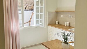 A modern kitchen with a wooden table, a potted plant, and a view of a stone wall through an open window. - Unique accommodation in Parakladi (Αγιος Νικολαος)