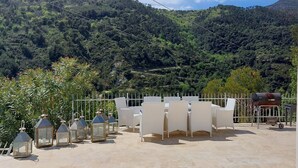 Une terrasse meublée de mobilier en osier et agrémentée de lanternes, offrant une vue sur une colline boisée.