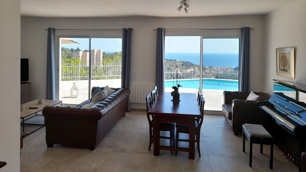 Un salon spacieux comprenant un piano, une table à manger et un canapé. De grandes fenêtres offrent une vue sur une piscine et la mer.