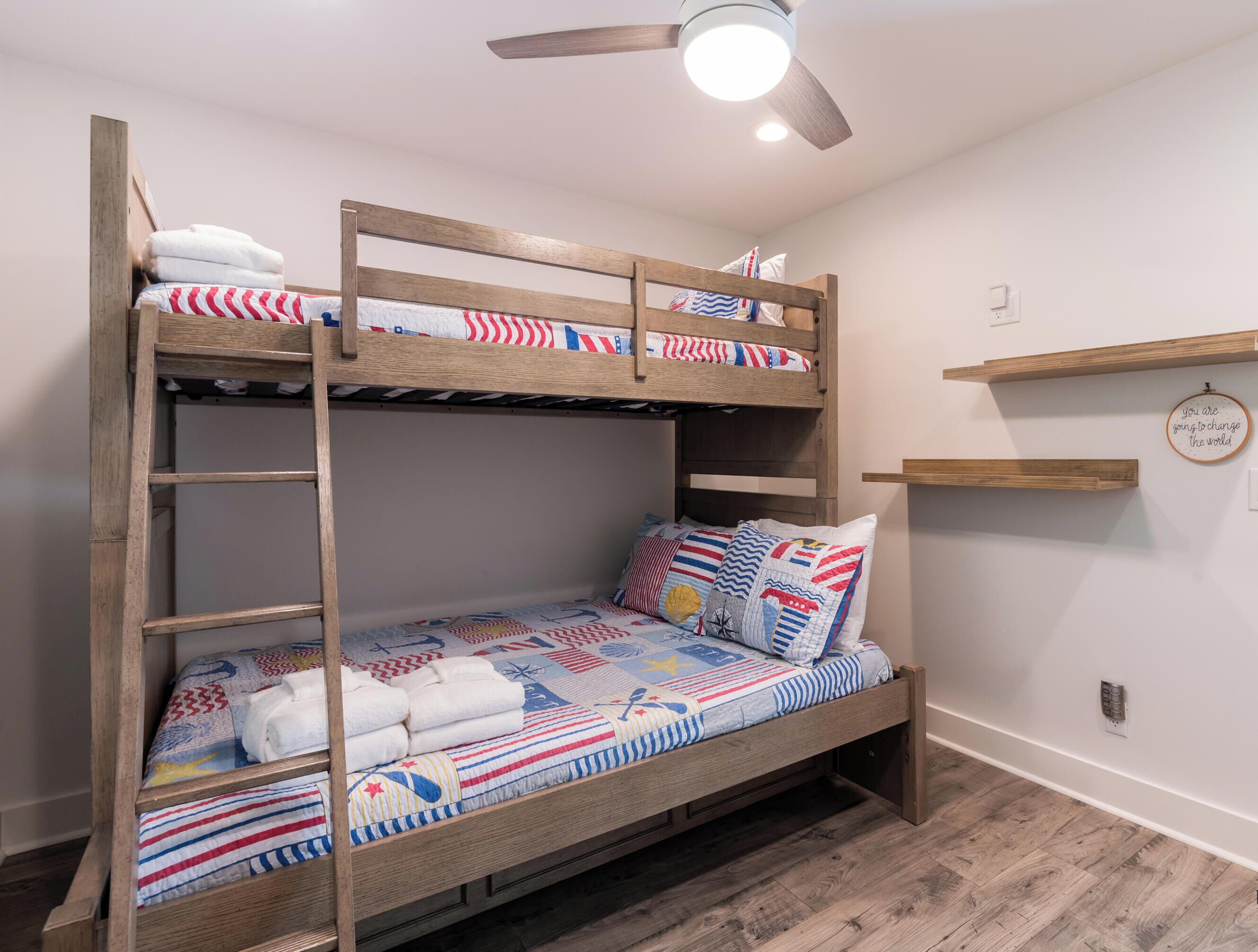 Una cama individual superpuesta con escalera, un ventilador de techo y una frase motivadora en la pared.