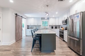 A modern kitchen with a central island, stainless steel appliances, and a farmhouse-style door. - 30 Forest Dr- Blue Oyster (Hilton Head Island)