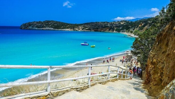 Eine Küstenansicht mit einer Treppe, die zu einem Strand führt, klarem blauen Wasser und Booten.