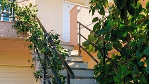 Eine Treppe mit Metallgeländer, umgeben von Grünpflanzen und einer Gebäudefassade.