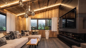 Ein modernes Wohnzimmer mit Holzvertäfelung, einem großen Flachbildfernseher, einer Couch, einem Couchtisch und hängenden Pendelleuchten.