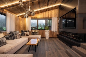 Una sala de estar moderna con detalles de madera, un televisor de pantalla plana grande, un sofá, una mesa de centro y lámparas colgantes.