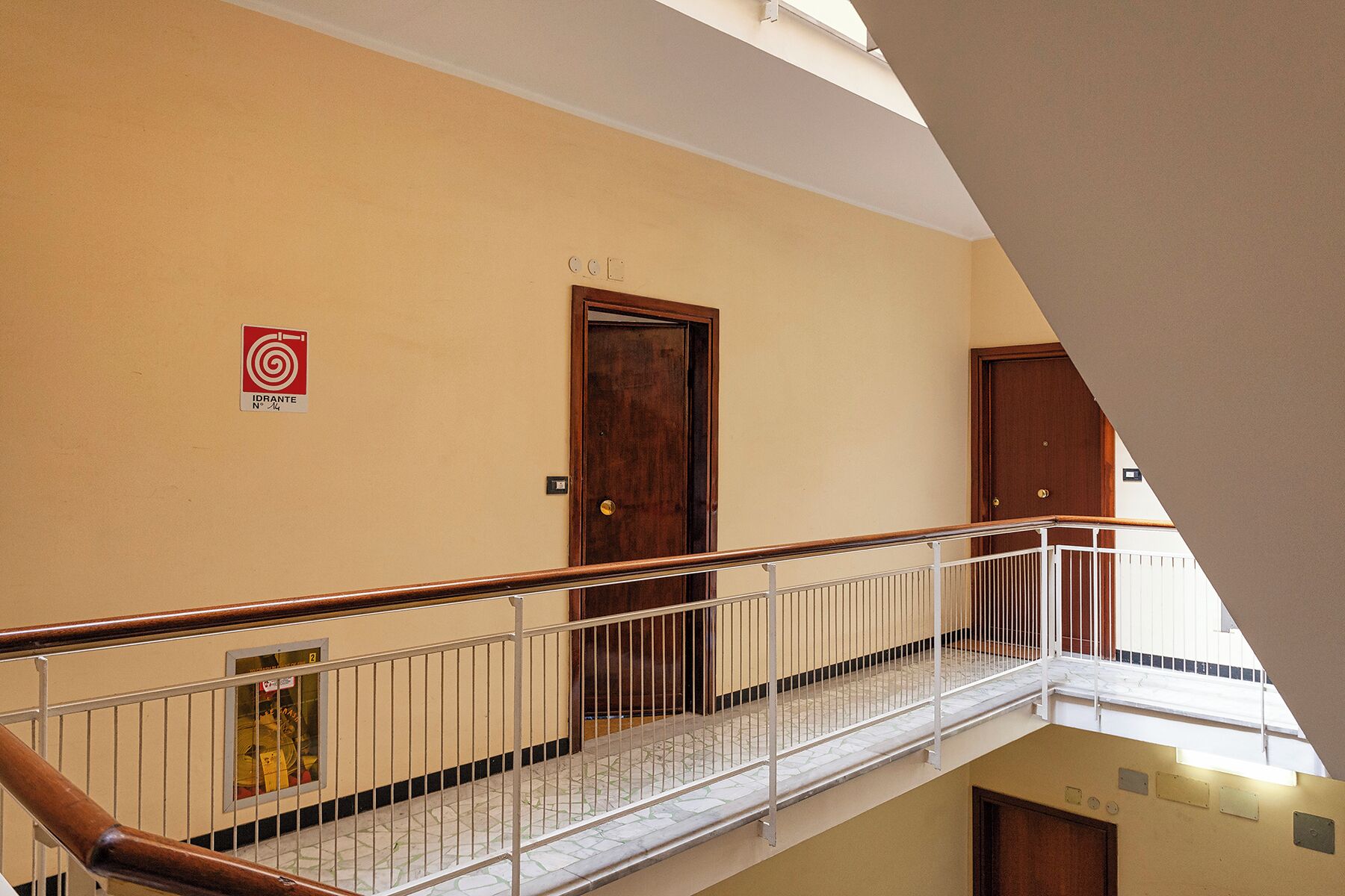 A multi-level interior with a wooden door, a red emergency exit sign, and a metal railing on the upper level.