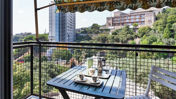 A balcony with a table set for tea, overlooking a cityscape with buildings and greenery. - Golden skyview from San Martino by Wonderful Italy (Genoa)