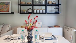 A dining area with a table set for four, a vase with red berries, and a shelf above containing kitchenware and a clock. - Golden skyview from San Martino by Wonderful Italy (Genoa)