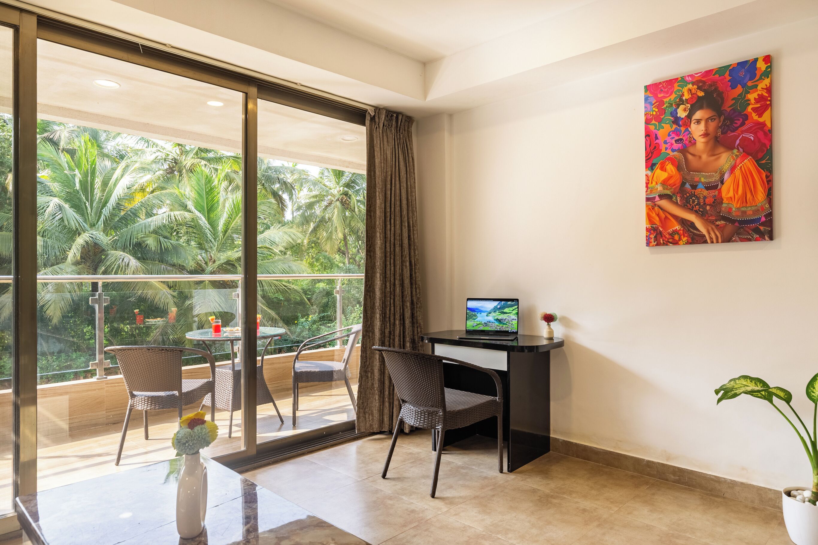 A modern room with a desk, laptop, and a large window overlooking a balcony with chairs and a plant.