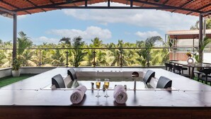 Un área de comedor al aire libre techada, con vista a palmeras y un cielo despejado.