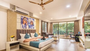 Habitación de hotel moderna con una cama grande, un escritorio y un balcón con vistas a zonas verdes.