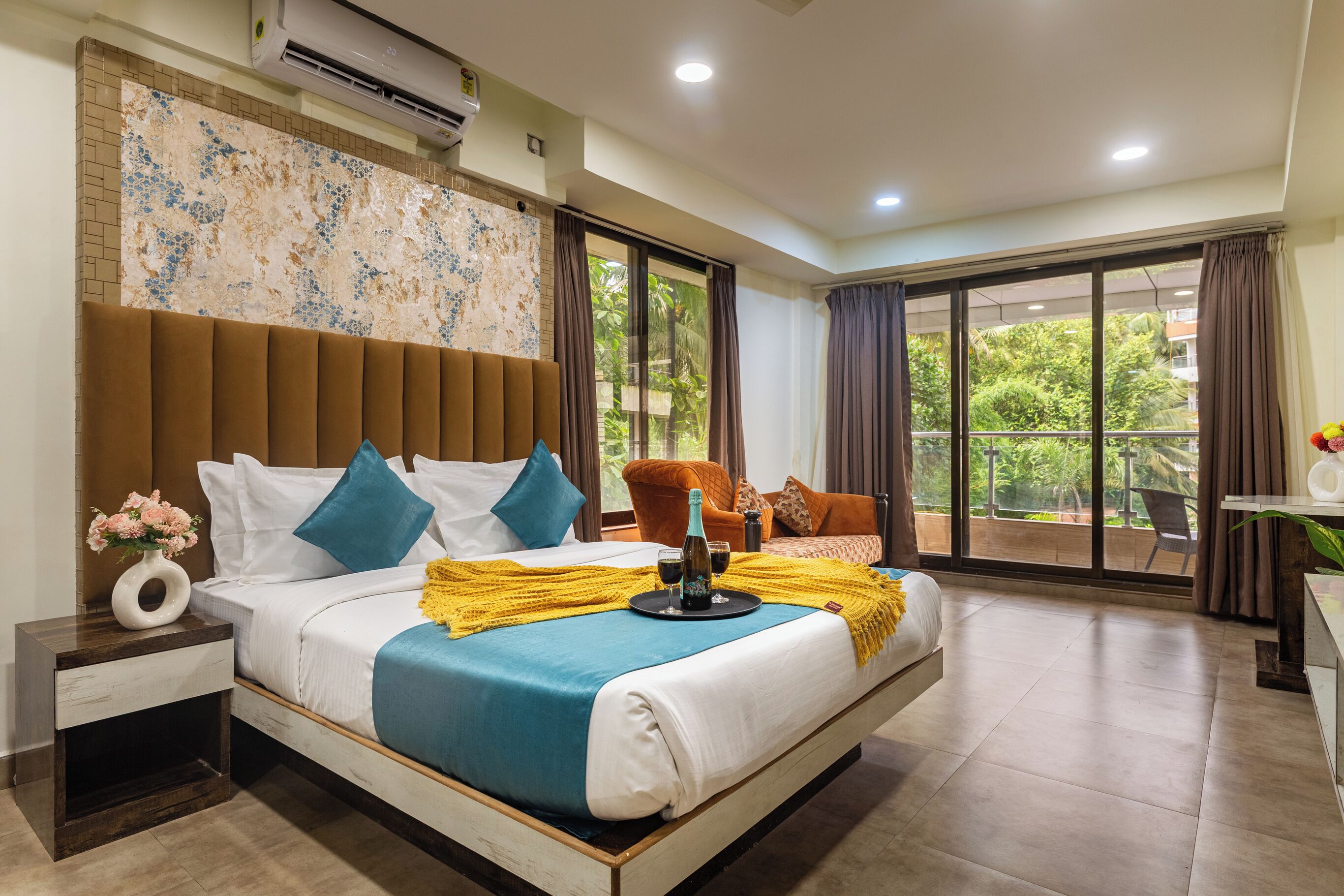 A spacious bedroom with a large bed, a nightstand, a window with curtains, and a balcony with a chair.