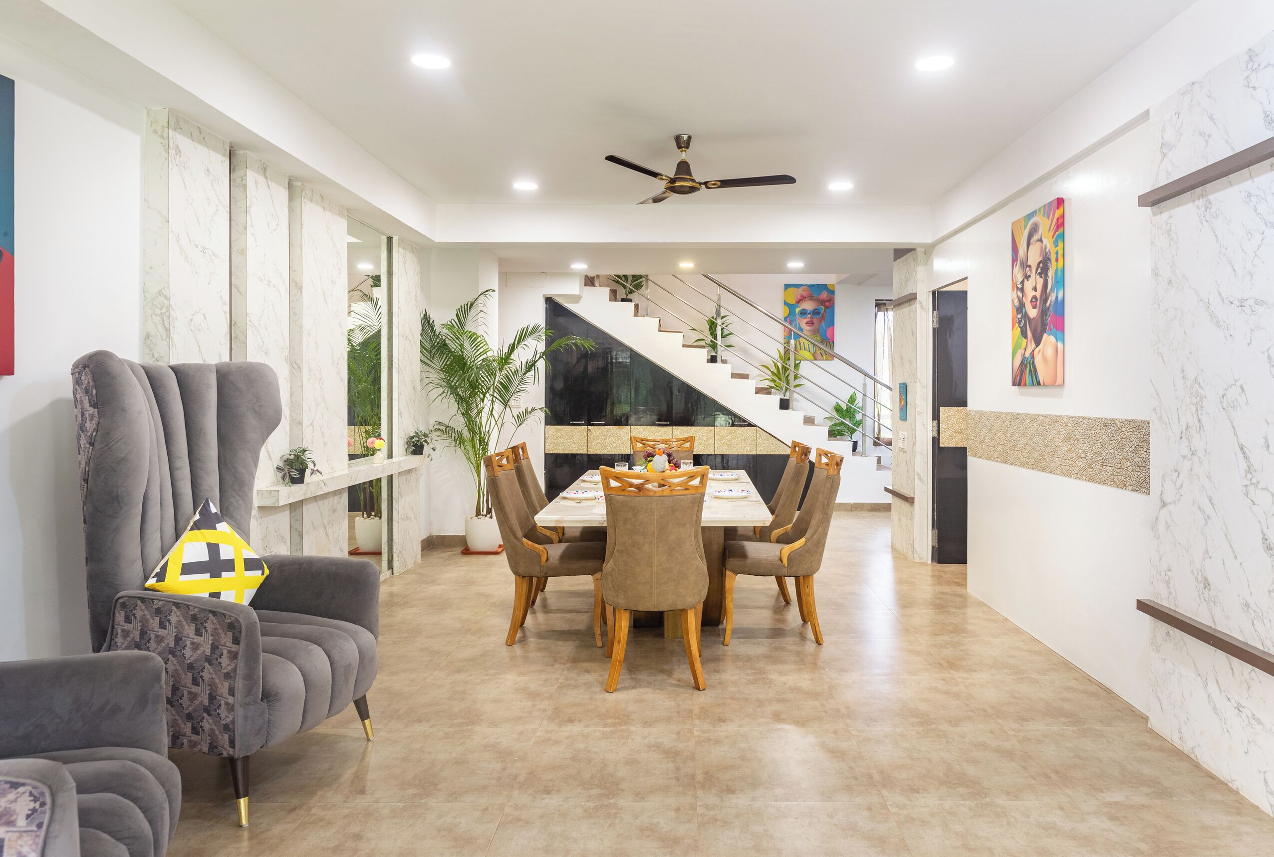 A modern dining area with a white table and chairs, a grey sofa, and a staircase leading to an upper level.