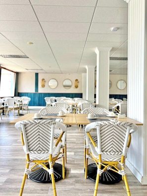 A dining area with wicker chairs and tables, a blue accent wall, and ceiling lights.
