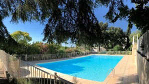 Une piscine rectangulaire, bordée d’une terrasse carrelée, entourée d’une clôture en métal et d’arbres.