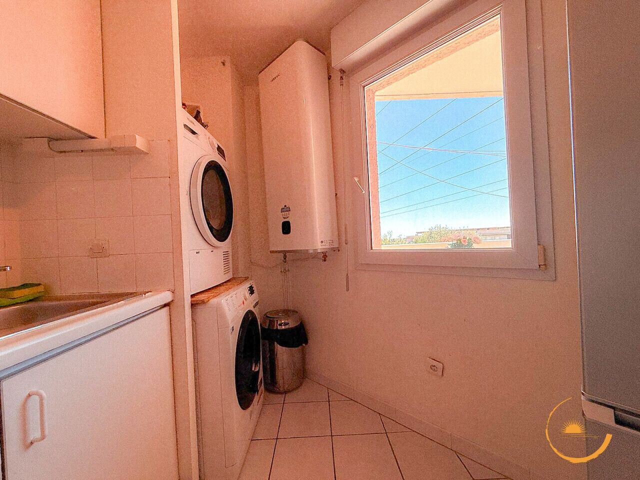 A compact laundry room with a washing machine, dryer, and a small trash bin.