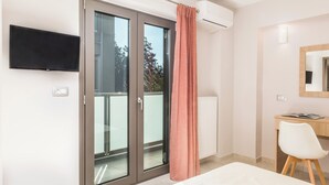 Un dormitori modern amb una porta corredissa de vidre que dona a un balcó, una televisió de pantalla plana penjada a la paret, un escriptori blanc amb una cadira i un mirall gran sobre l'escriptori.