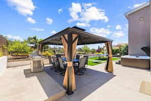 Un patio exterior con una pérgola, una parrilla y asientos.