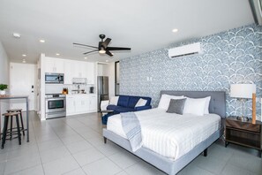 Een moderne slaapkamer met een groot bed, een blauwe bank en een kitchenette op de achtergrond.