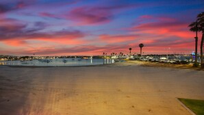 Una spiaggia con un cielo al tramonto, acqua calma e un'area parcheggio con palme.