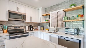 Une cuisine moderne avec des armoires blanches, un grand îlot central, un four encastré, un four à micro-ondes, un grille-pain et un lave-vaisselle.